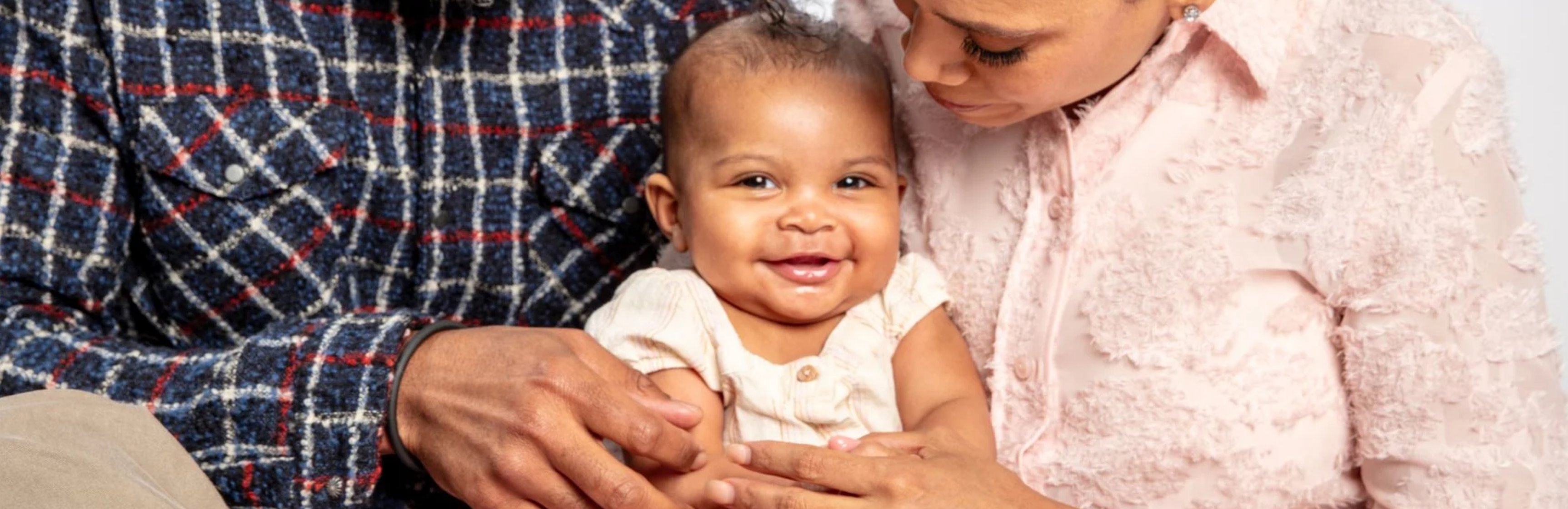 Foto de una bebé afroamericana sonriendo y en brazos de sus padres