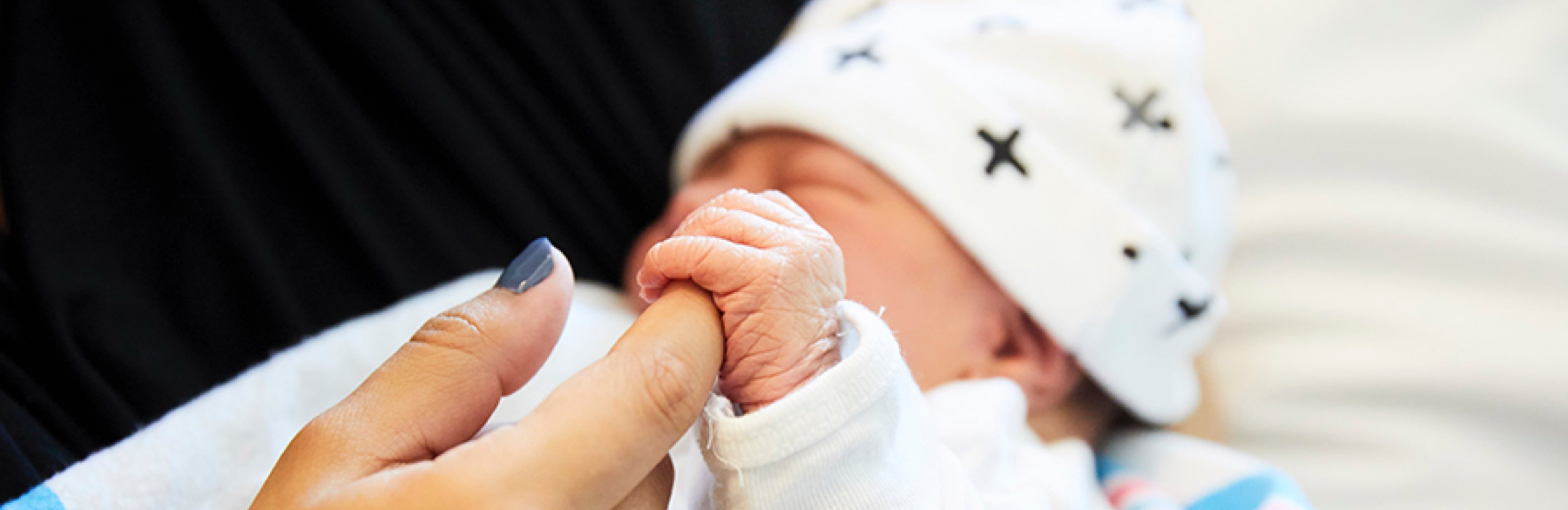 Newborn baby with black hair sleeps on a blanket wearing a hospital bracelet