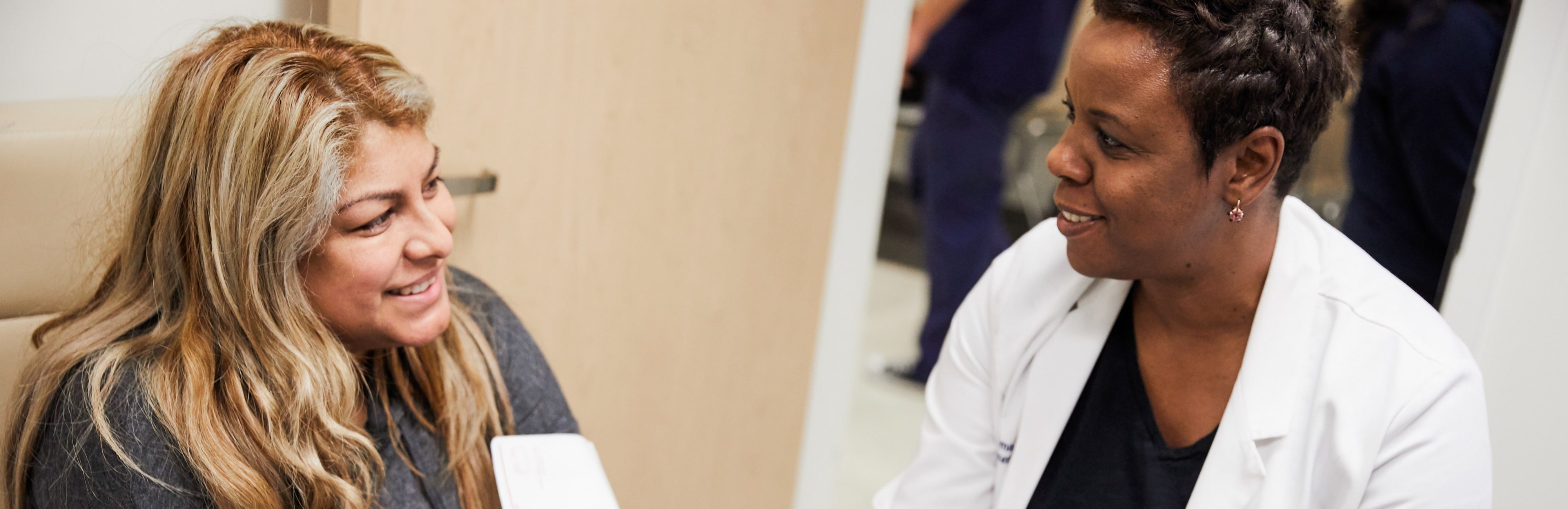 Latina female patient smiling at Black female doctor in white coat