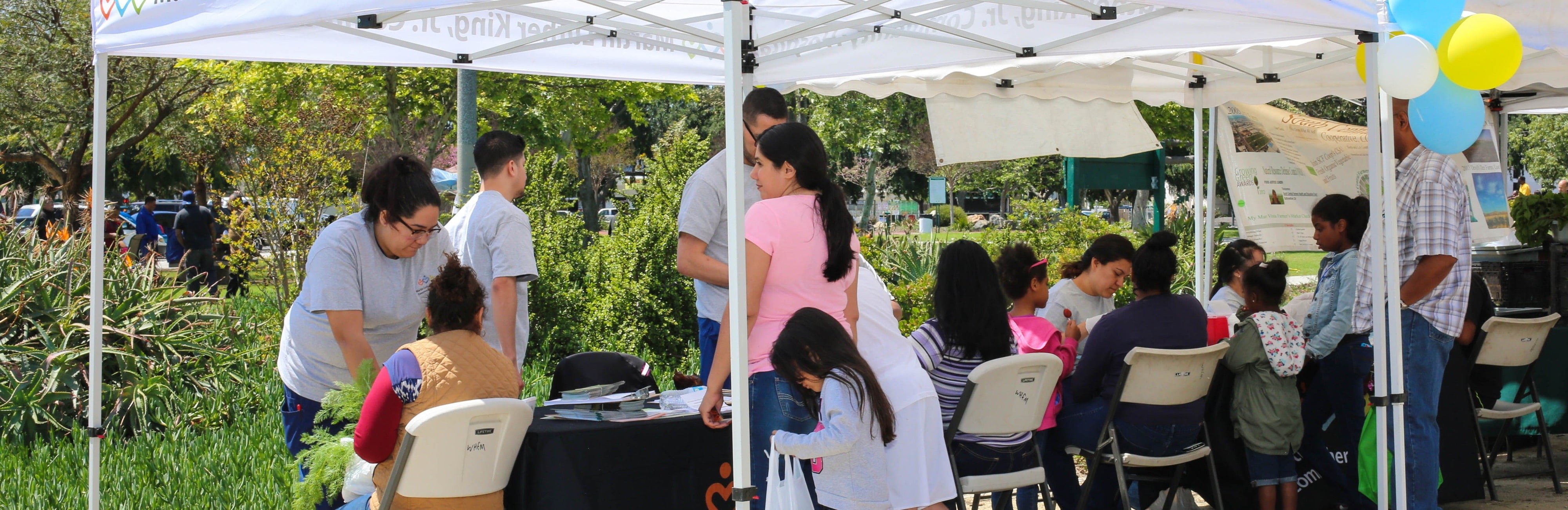 South LA community members sitting under pop up tent and speaking to community health workers 