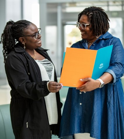 Photo of two AA women talking and holding a folder